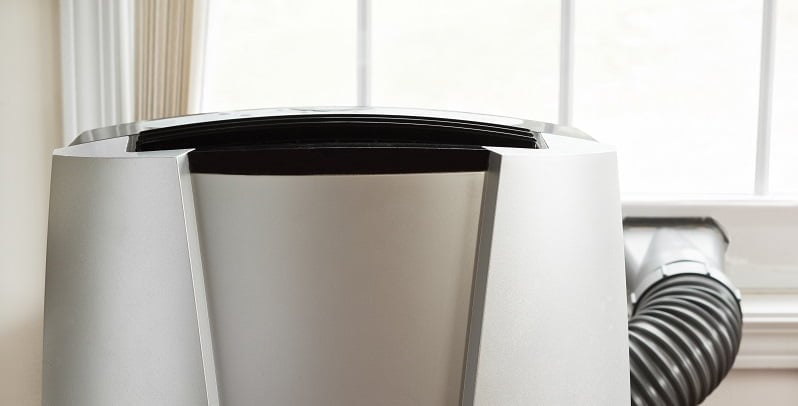 dual hose Portable air conditioner in front of brightly lit window.