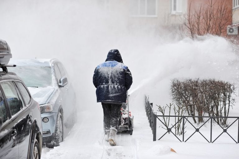 man removes snow in the yard of a multistory building with snow machines