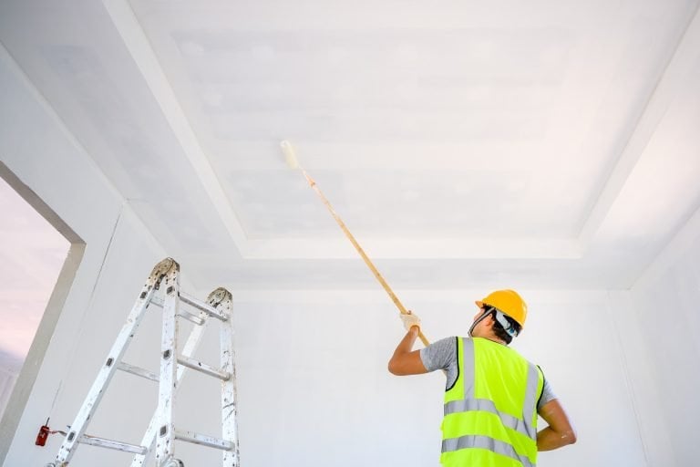 Young Asian male construction worker Work as a house painter Painting the ceiling inside the house and using a white primer paint roller on the construction site. How To Paint A Ceiling With A Roller.